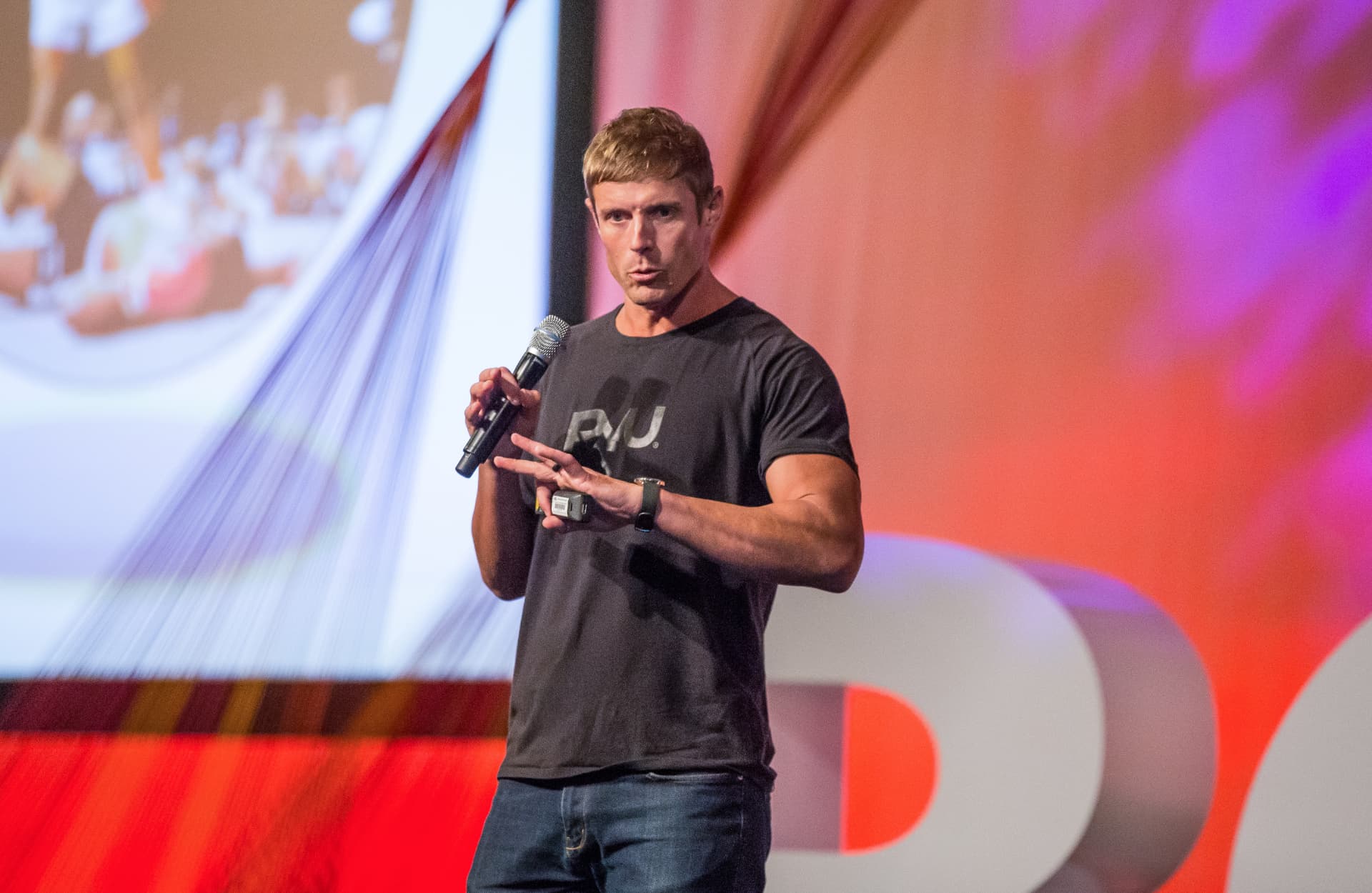 Dai Manuel speaking on stage with a microphone at a Mindbody event