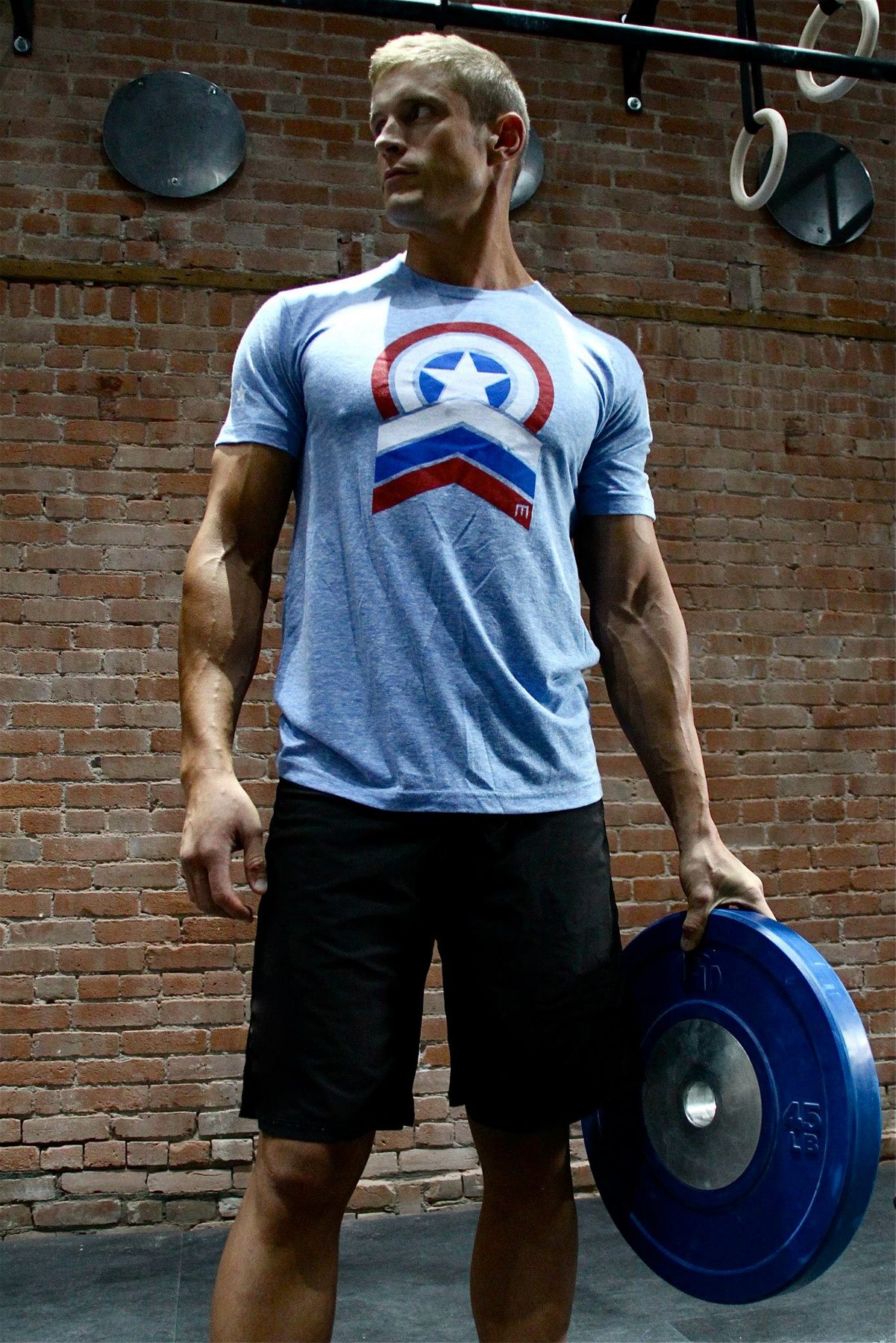 Dai Manuel carrying a weight plate in a brick walled gym